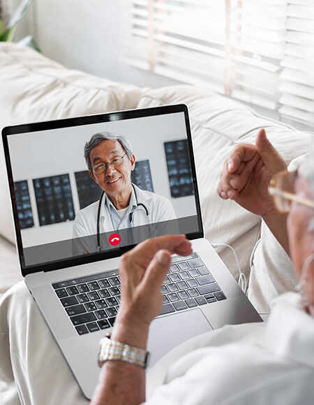 An elderly person having a video call with a doctor on a laptop.